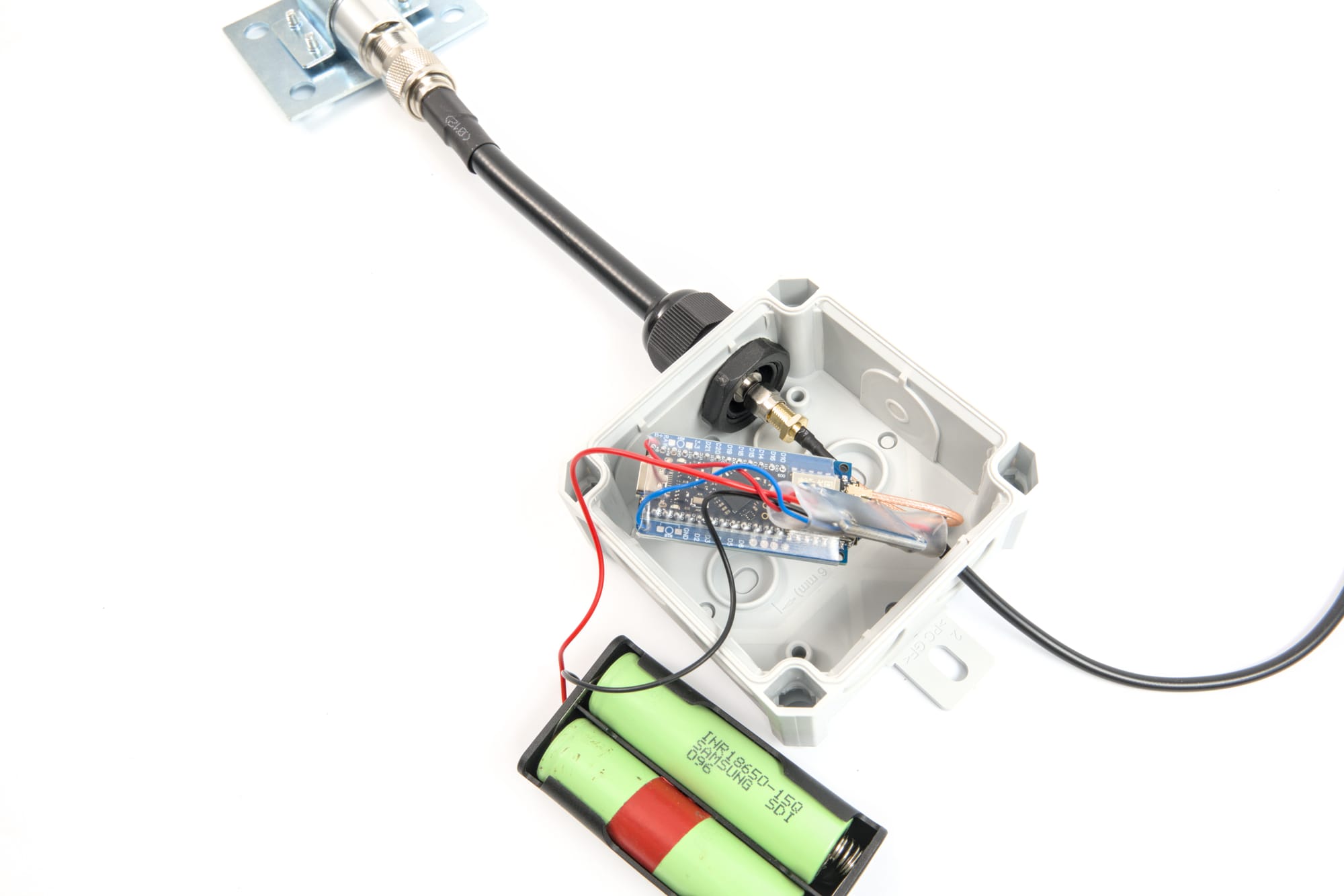 A cable gland routing a coax cable with N-to-SMA adapter through the wall of a Meshtastic node junction box.