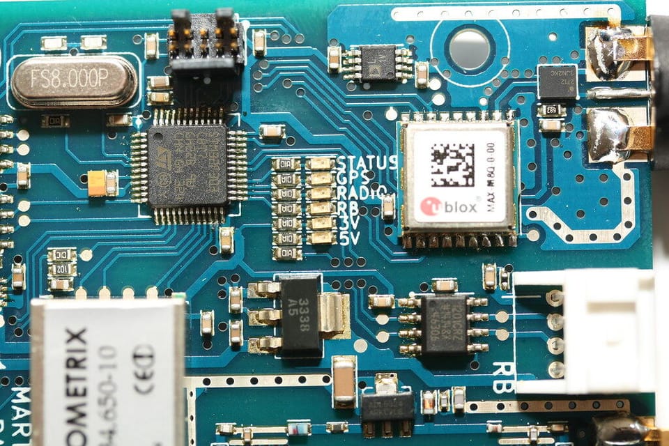 Close-up of a teal circuit board showing a u-blox GPS radio module with STATUS, GPS, and RADIO labels in the silkscreen